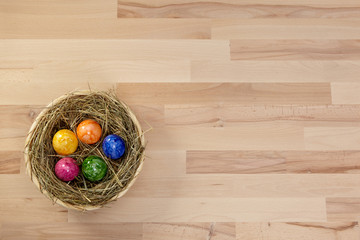Korb mit Heu und bunten Eiern auf Holz aus Buche