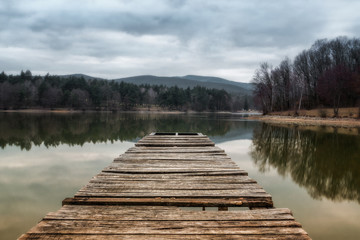 Fototapeta premium Lake pier at evening with hills on background. Reflection of the forest in the green water with blue cloudy sky. Pond at the forest. Small lake inrecreational area (Slovakia - Duchonka)