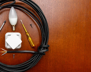 wire and electric tools, a light bulb, a socket, a screwdriver, a top view on the wooden table. Place for text. Flat lay. Top view