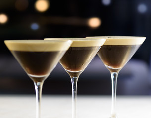 Drei Cocktails in braun und weiß in einer Reihe vor dunklem Hintergrund