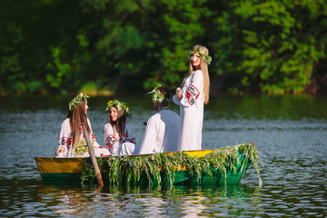 Midsummer. A group of young people in national costumes sail in a boat that is decorated with...