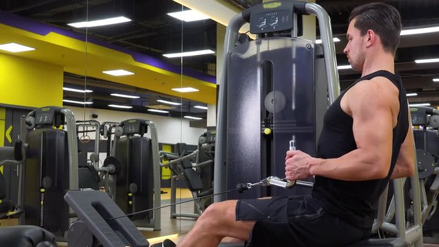 A young fit man trains on a rowing machine in a gym - view from the side
