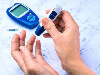 Diabetes checking blood sugar level. Woman using lancelet and glucometer at home
