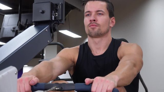 A young fit man trains on a rowing machine in a gym - closeup