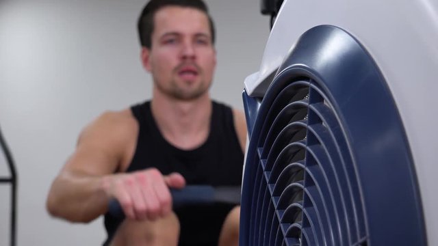 A young fit man trains on a rowing machine in a gym - closeup
