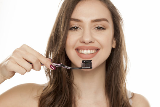 young woman holding a black tooth paste with active charcoal, and black tooth brush on white background