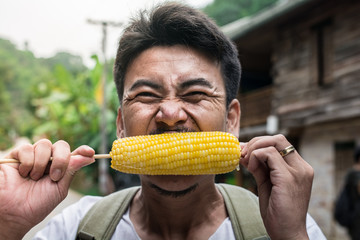 Man tourists with backpacks happily eat ripe corn traveling in Asia