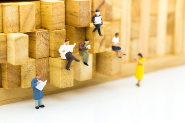 Miniature people: businessman reading newspaper on wooden block. Image use for background education or business concept.