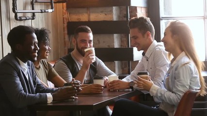 Multi-ethnic friends laughing having fun at meeting in coffeehouse, african and caucasian male buddies giving high five after telling good funny joke, multiracial young people hanging out in cozy bar