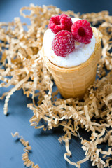 Ice cream with raspberry in waffle cone on wood