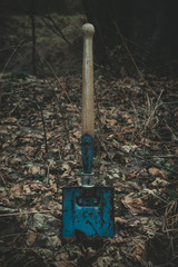 Old soviet military shovel in forest  sticking to the ground. Old vintage and retro wooden and blue military shovel.