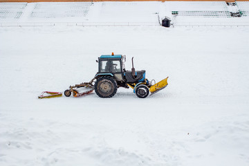 Cleaning tractor snowballed football field in winter