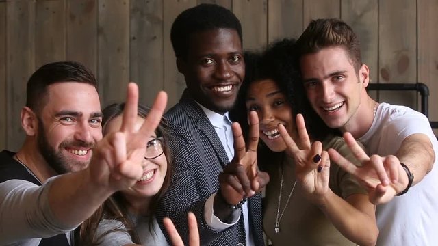 Diverse happy young people posing for making group photo, smiling multi-ethnic students showing peace sign while taking picture, black and white friends capturing moment looking at camera