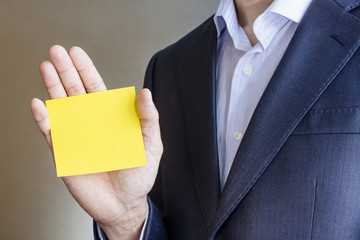Business man in suit, holding in hand yellow Paper card for text. Copy space