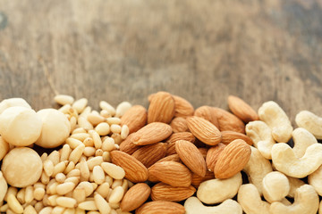 A bunch of almonds , macadamia nuts, pine nuts, cashews on an old brown wooden table, copy space