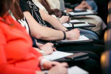 Close up students sitting at the desk at the lecture hall taking notes at notebooks. Education process.