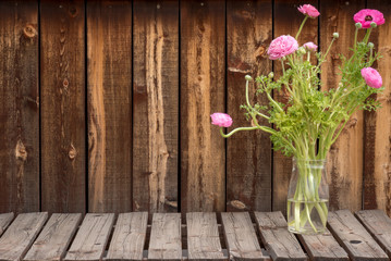 Bunch of bright pink ranunculus flowers in a clear vase on a rustic plank table.