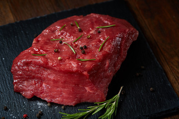 Raw meat beef steaks on black slate board with spices and rosemary over wooden background, copy space