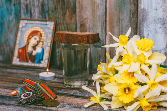 celebration of victory day on may 9, 1945, medals, Orthodox icon and a burning candle, a bouquet of Narcissus flowers, and a glass of vodka with a piece of rye bread on the table