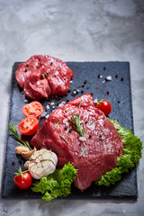 Composition of raw beefsteak on slate board with vegetables and seasoning, selective focus, close-up.