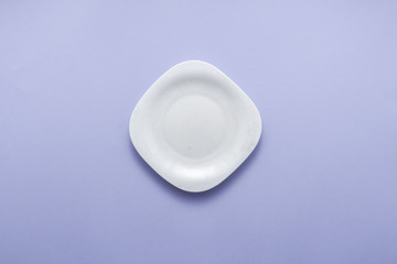 Single empty plate on purple background top view flat lay