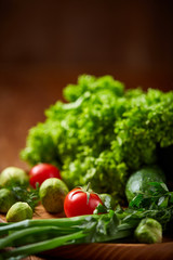Vegetarian still life of fresh vegetables on wooden plate over rustic background, close-up, flat lay.