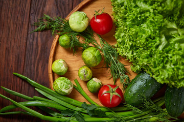 Vegetarian still life of fresh vegetables on wooden plate over rustic background, close-up, flat lay.