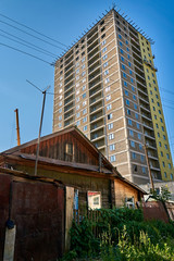 Old wooden house in front of a big tall modern skyscraper