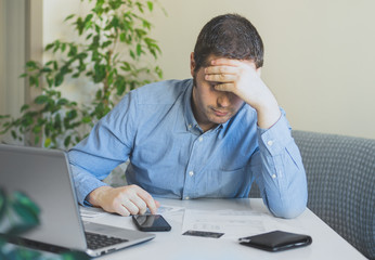 Sad man looking at his monthly bills at home.