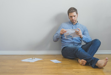 Fototapeta premium Handsome man sitting at the floor and looking at his bills.