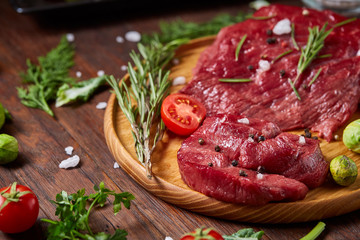 Flat lay of raw beefsteak with vegetables, herbs and spicies on metal tray, close-up, selective focus