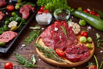 Flat lay of raw beefsteak with vegetables, herbs and spicies on metal tray, close-up, selective focus