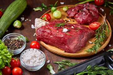 Flat lay of raw beefsteak with vegetables, herbs and spicies on metal tray, close-up, selective focus