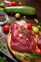 Flat lay of raw beefsteak with vegetables, herbs and spicies on metal tray, close-up, selective focus