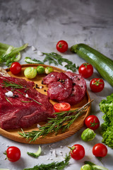 Still life of raw beef meat with vegetables on wooden plate over white background, top view, selective focus