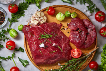 Still life of raw beef meat with vegetables on wooden plate over white background, top view, selective focus
