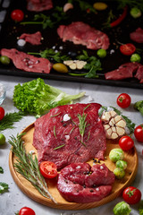 Still life of raw beef meat with vegetables on wooden plate over white background, top view, selective focus