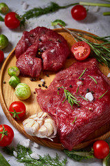 Still life of raw beef meat with vegetables on wooden plate over white background, top view, selective focus