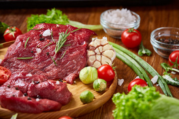 Still life of raw beef meat with vegetables on wooden plate over white background, top view, selective focus