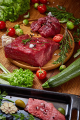 Still life of raw beef meat with vegetables on wooden plate over white background, top view, selective focus