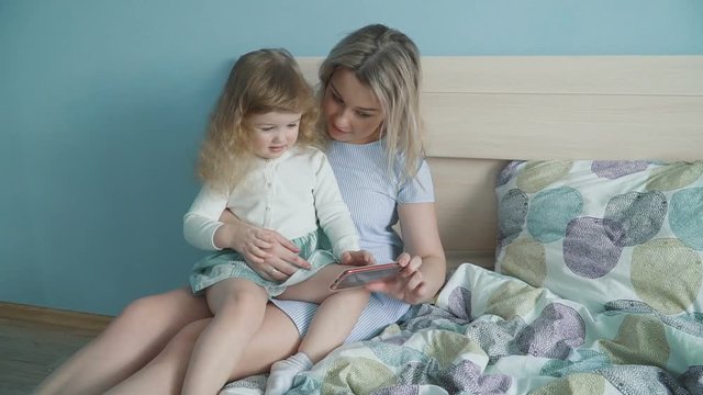 Mother and her cute little daughter watching photos in the photo albumon the bed. Slow motion family concept video.
