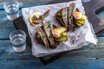 Vodka and a set of sandwiches with sprats on a wooden background. Top view. Copy space