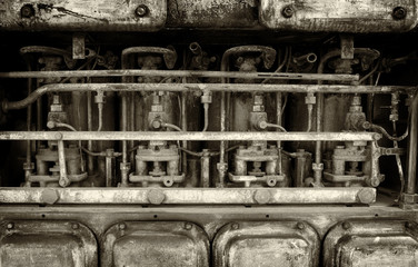 monochrome image of a big old old rusting petrol engine with details of pipes bolts and cylinders