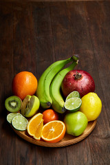 Ripe fresh fruits in a wooden plate on a light wooden background, selective focus, close-up, top view