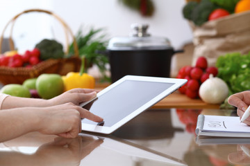 Closeup of human hands cooking in kitchen. Women discuss a menu using tablet computer. Copy space area at touch pad. Healthy meal, vegetarian food and lifestyle concepts