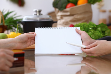 Closeup of human hands cooking in kitchen. Women discuss a menu using block note. Copy space area. Healthy meal, vegetarian food and lifestyle concepts
