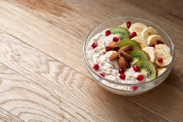 Delicious oatmeal porrige with fruits in glass bowl over white textured background, selective focus, flat lay, close-up.