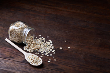 Overturned glass jar and spoon with raw oatmeal on vintage wooden background, close-up, selective focus.