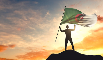 Algeria flag being waved by a man celebrating success at the top of a mountain. 3D Rendering - obrazy, fototapety, plakaty