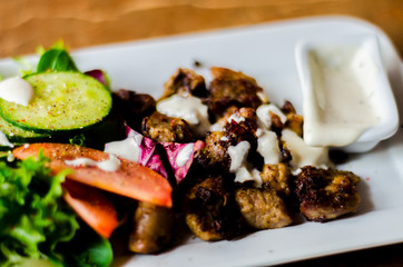 tasty dish with pork, lettuce, tomato and cucumber on a white plate with a dip